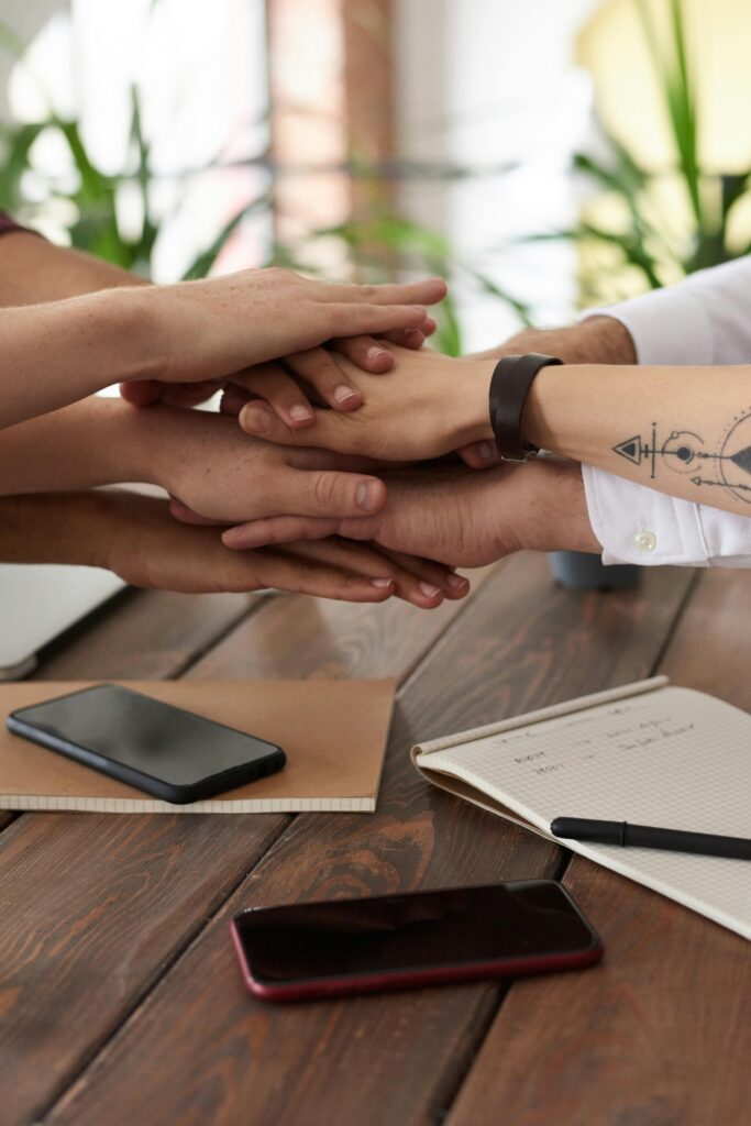 Hands from a diverse team stack on a table symbolizing unity and teamwork in a modern office setting.